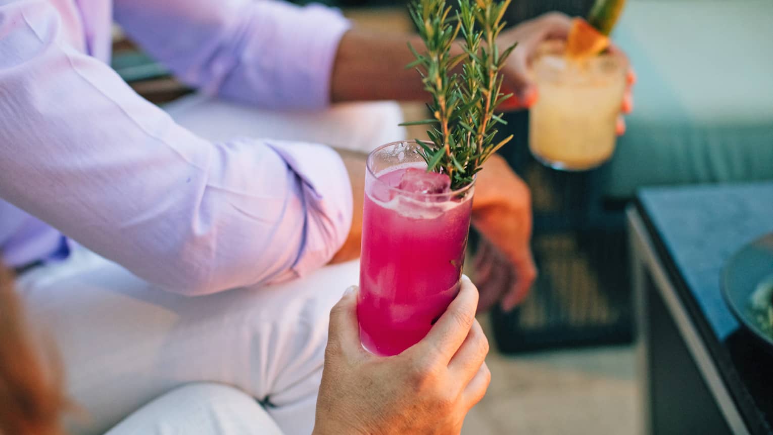 Two people holding bright cocktails.