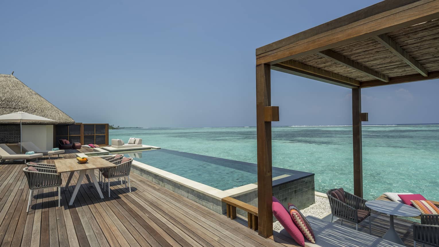 Large wooden deck with dining table and infinity pool overlooking clear turquoise water