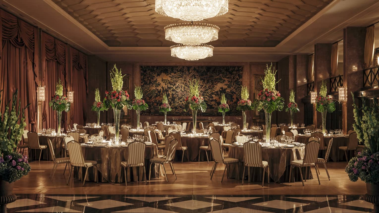 Art Deco-style dining room with tiles, banquet tables with tall flower arrangements, crystal chandelier 
