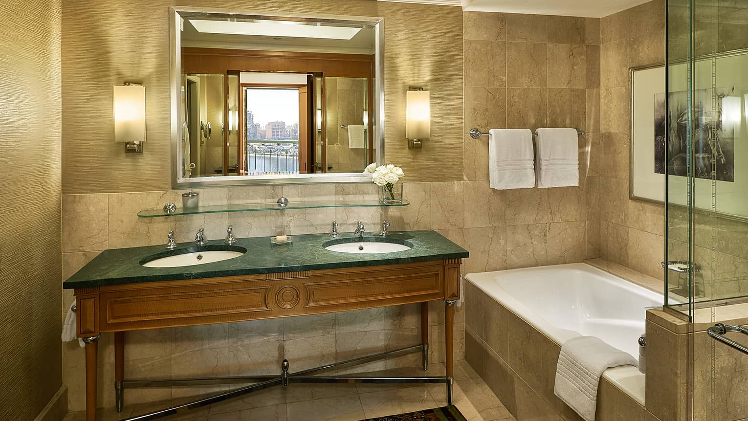 Guest room bathroom with double green granite?topped vanity, deep soaking tub,  mirror flanked by lighted wall sconces, glass shower