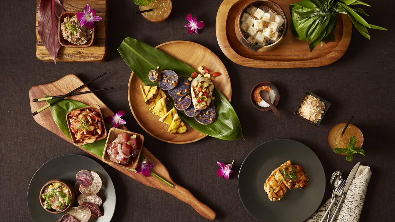 Aerial view of wooden bowls with contemporary food, garnished with large leaves, orchids and chopsticks