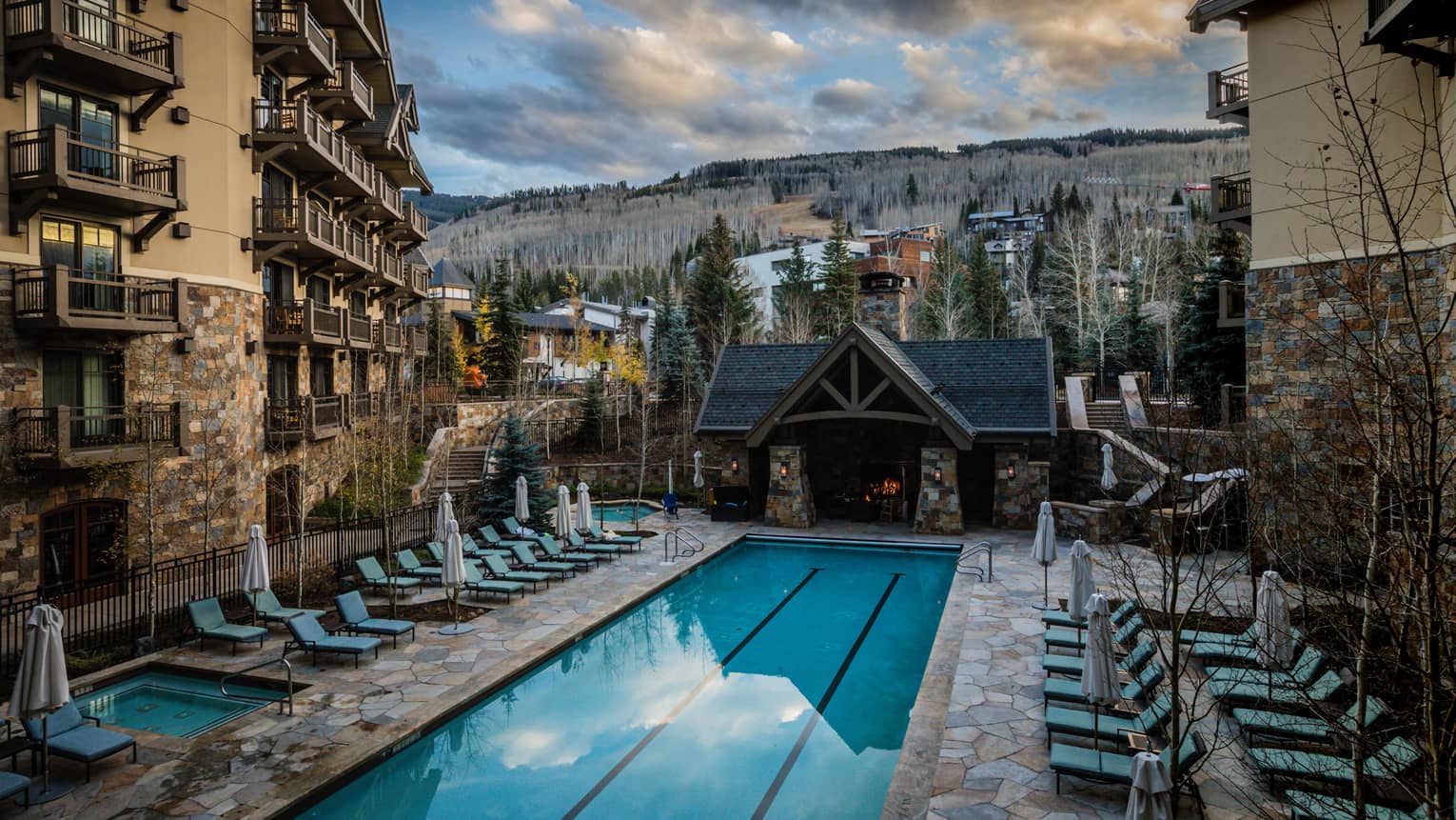Blue lounge chairs face rectangle heated pool, surrounded by hotel building and mountain views