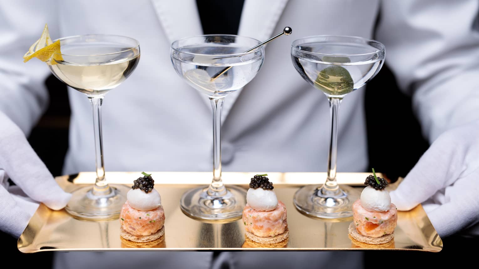 Hotel staff holding brass tray with three martinis, small canapes with caviar