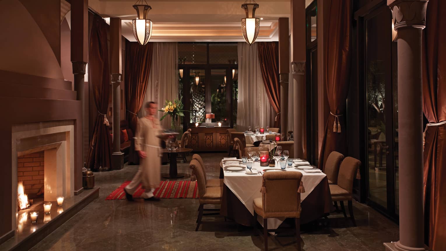 Arancino room, staff carries tray towards private dining table by fireplace 