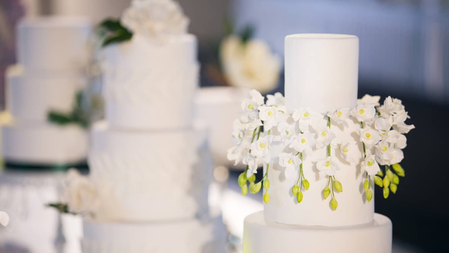 Three-tiered wedding cakes are each garnished with white florals 