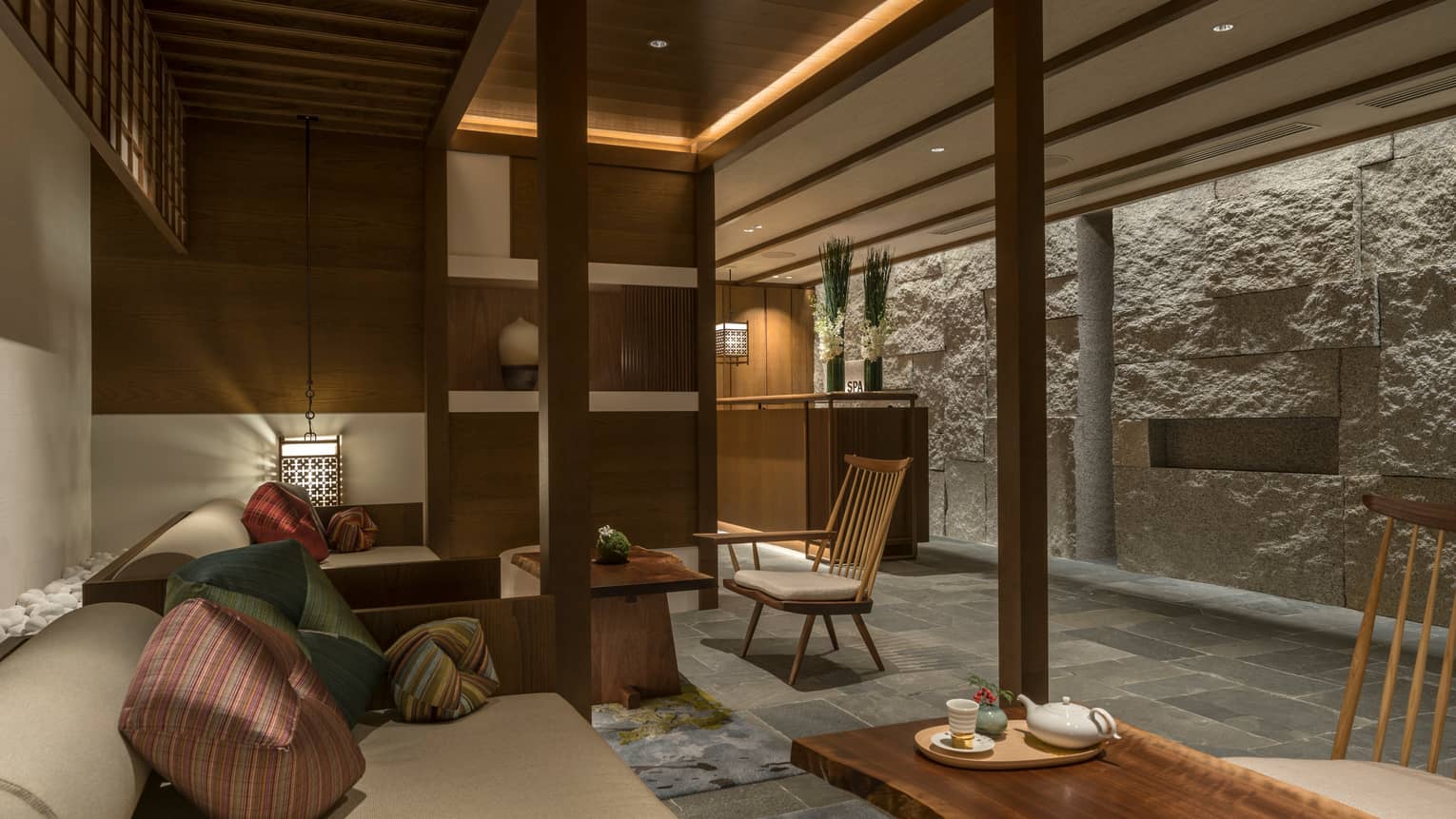 Spa lounge with plush bench, cushions, tea on table, lanterns, rock wall