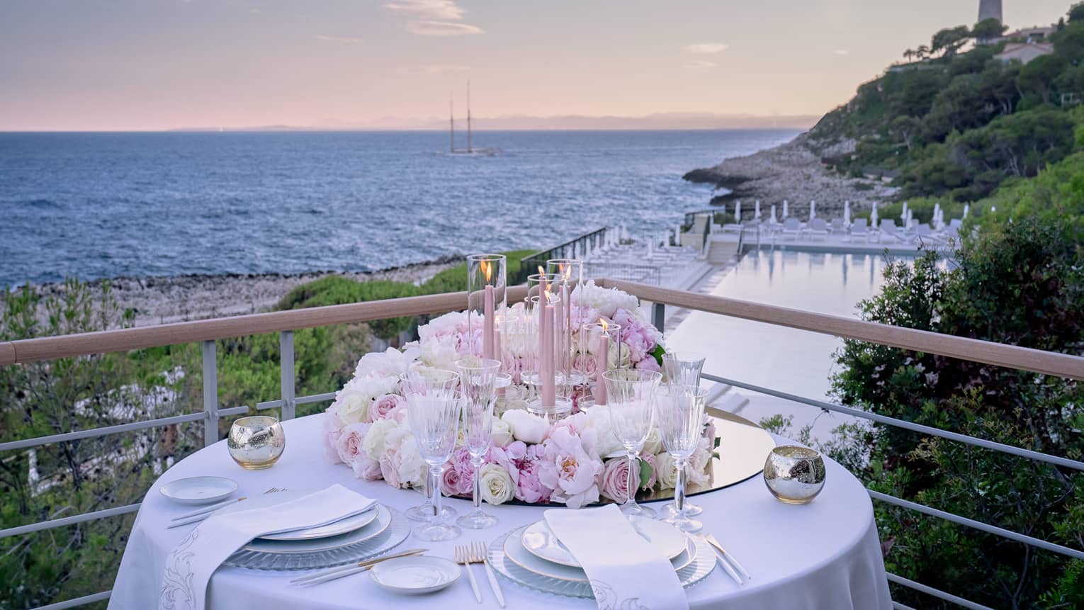 Balcony with round set table, pink floral arrangement, water views at sunset