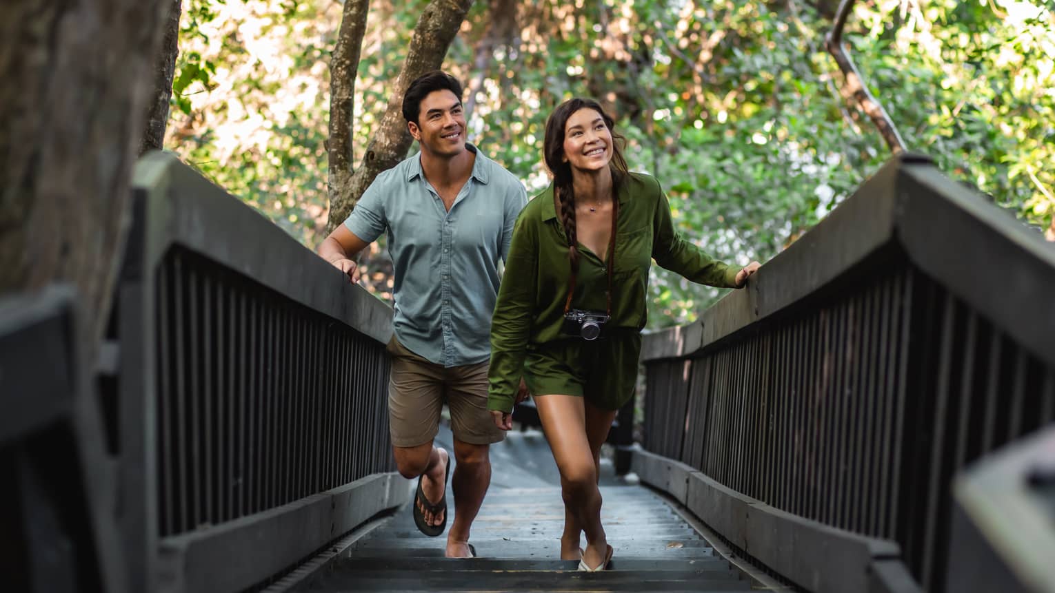 A man and a woman walk up a wooden walkway surrounded by trees