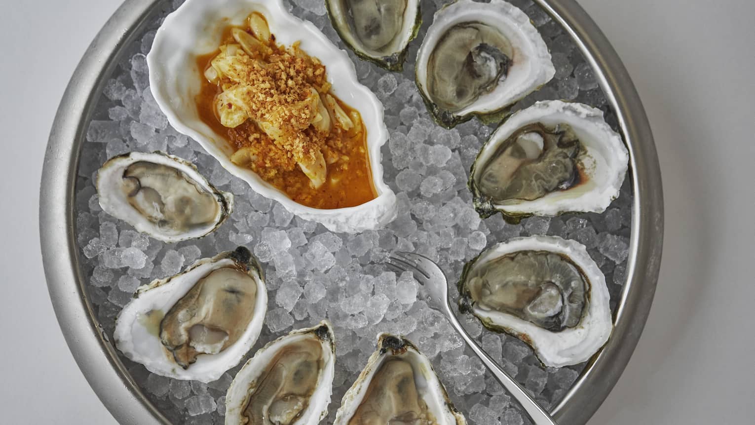 An aerial view of fresh oysters on a plate of ice with a red sauce to the side