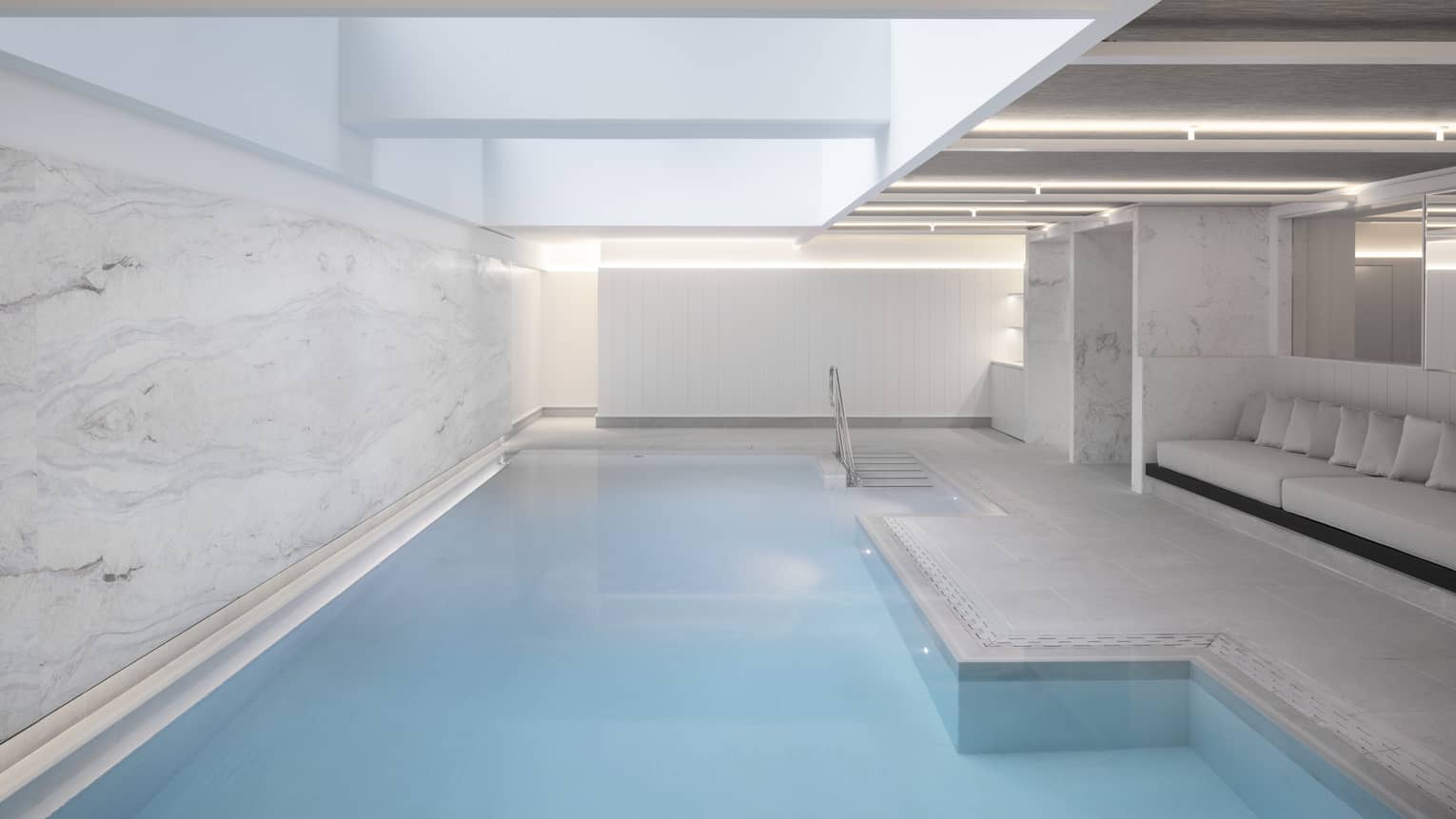 Indoor pool at spa, banquet of seating on one side, marbled wall on other 