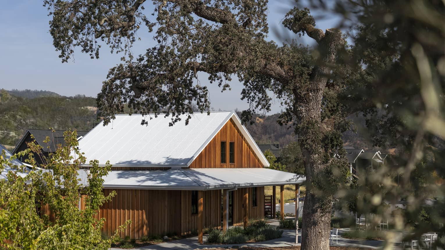 A wood building behind trees and surrounded by plants.