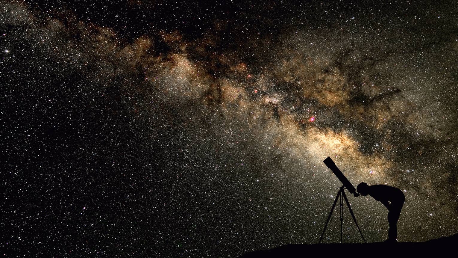 Silhouette of stargazer leaning into telescope against a starry sky, milky way