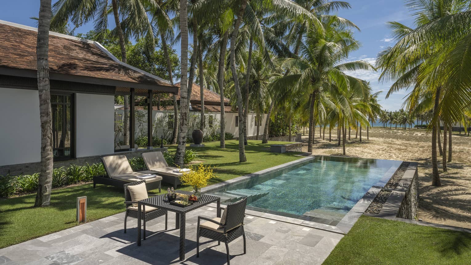 One Bedroom Pool Villa pool area with lounge chairs, two-seater table, palm trees and sunshine