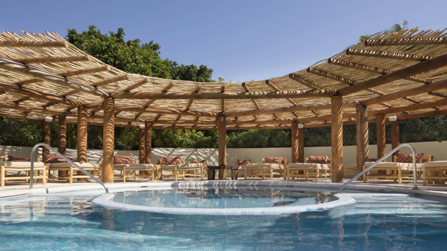 Resort pool with two entries and lounge chairs under thatched-roof awning