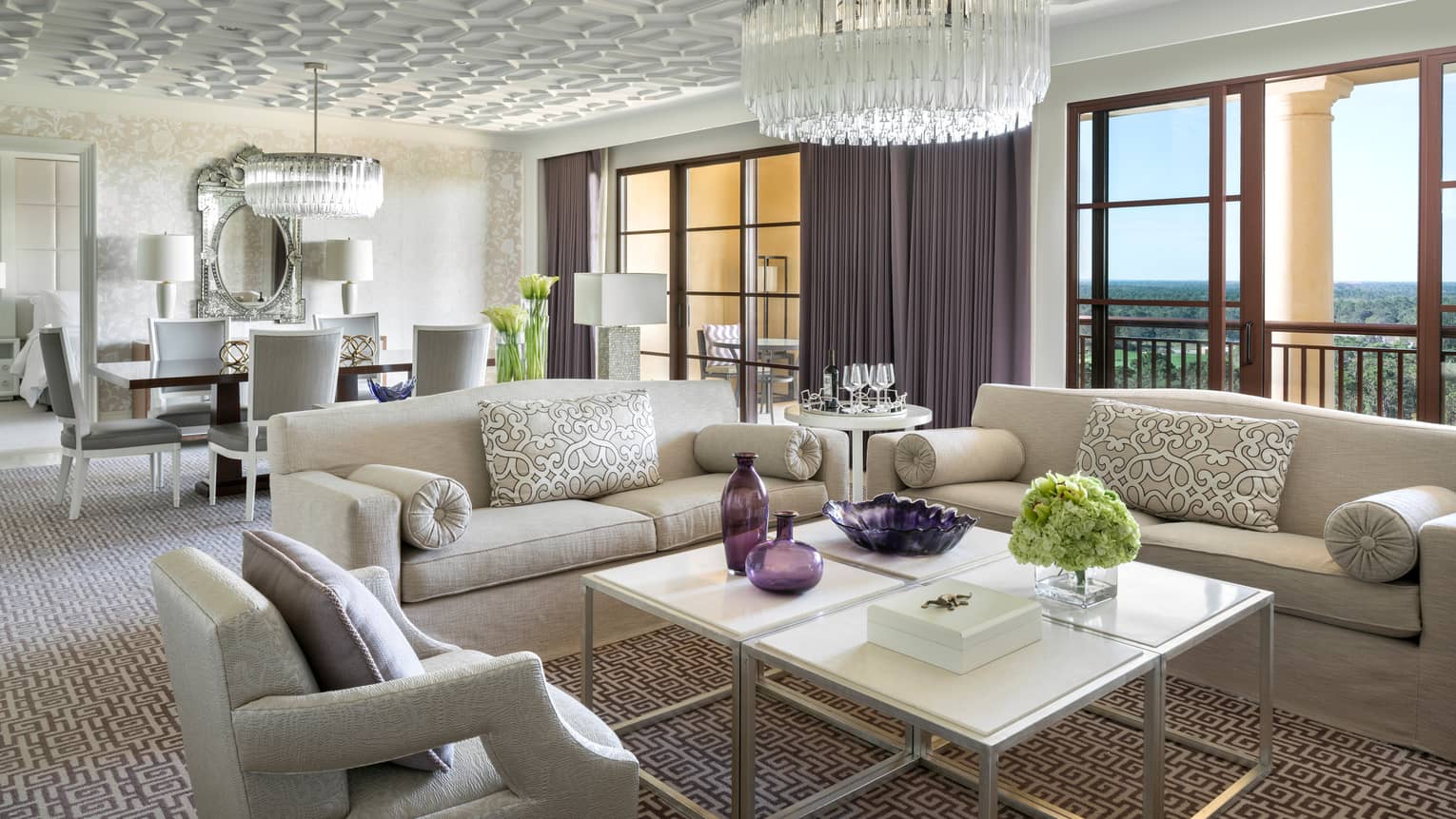 Grand Suite white sofas, armchair around coffee table with purple vases under crystal chandelier, sunny windows