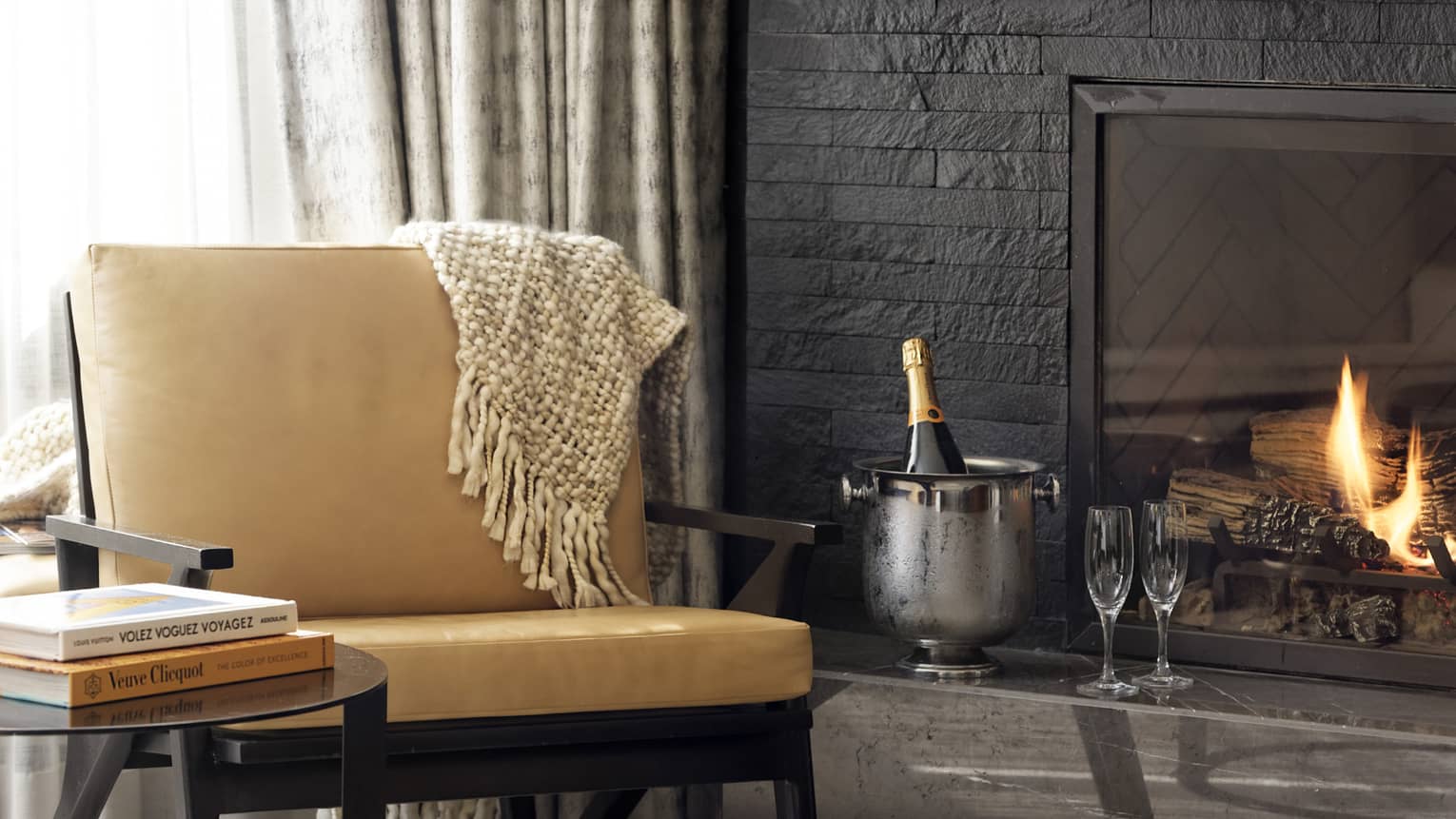 Leather chair, round side table, fireplace, ice bucket with bottle of champagne and two flutes