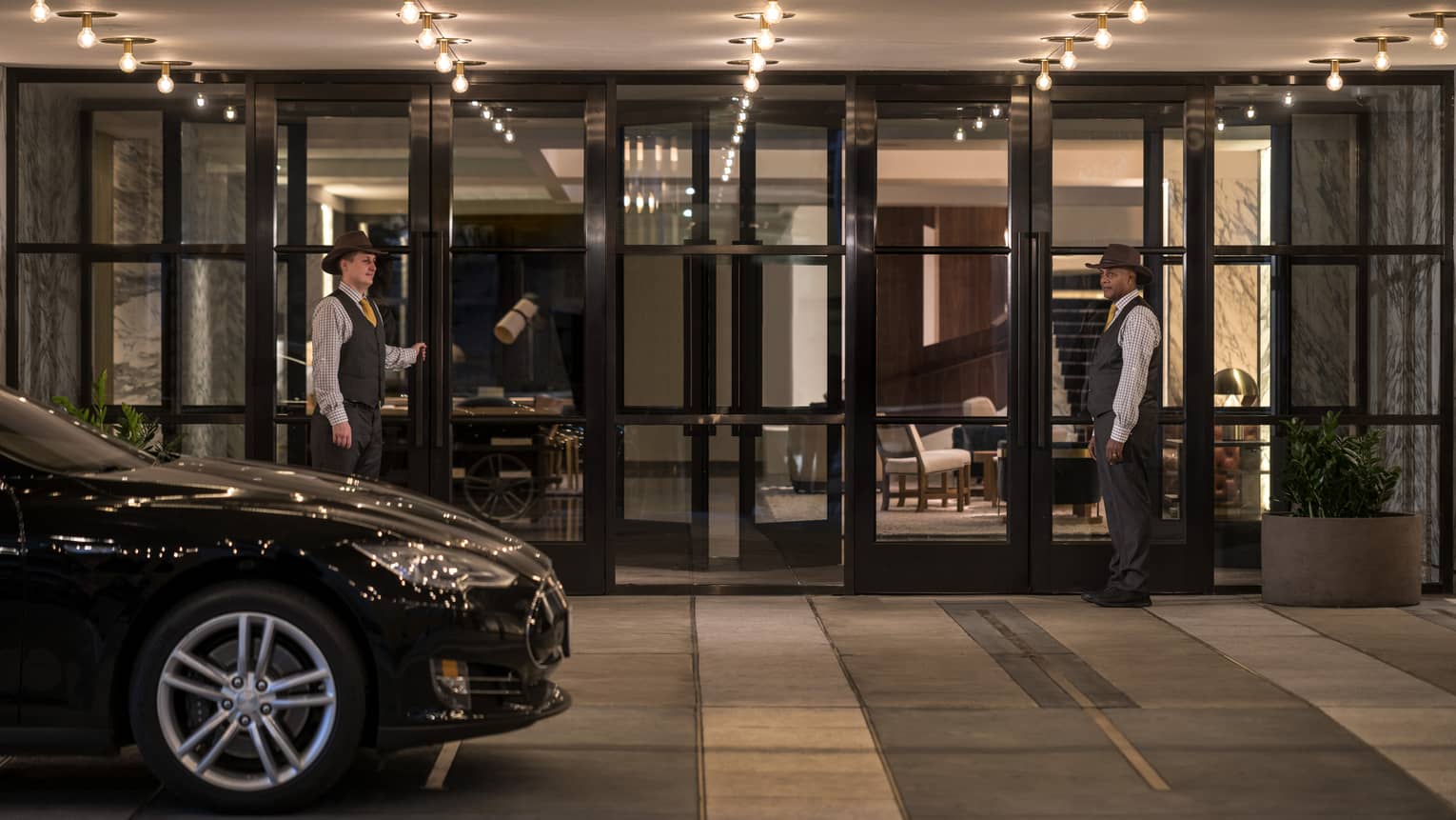 A car pulling up to the valet entrance of a hotel with two team members standing by glass doors.
