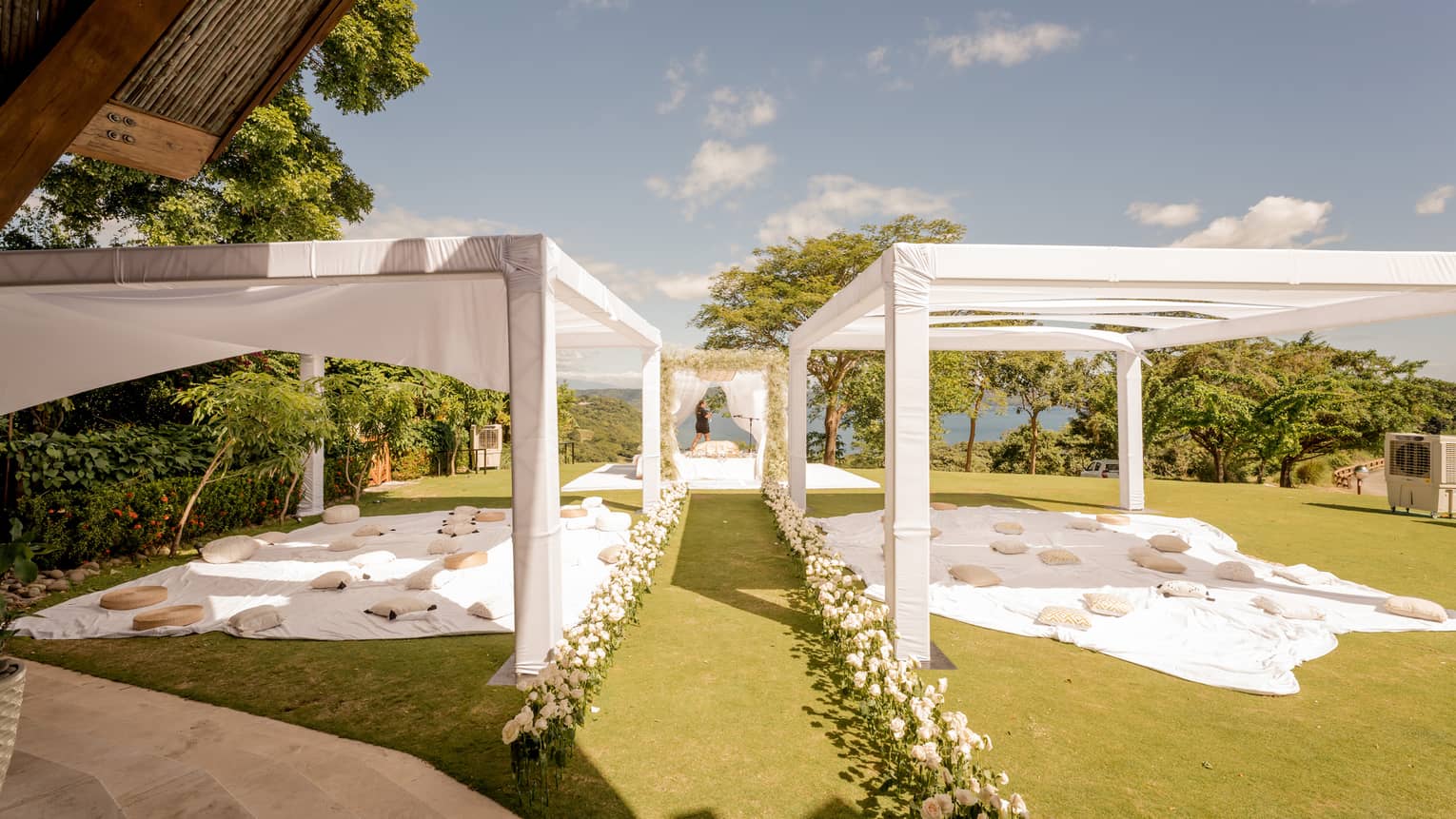 Covered wedding reception area on green lawn, aisle decorated with flowers