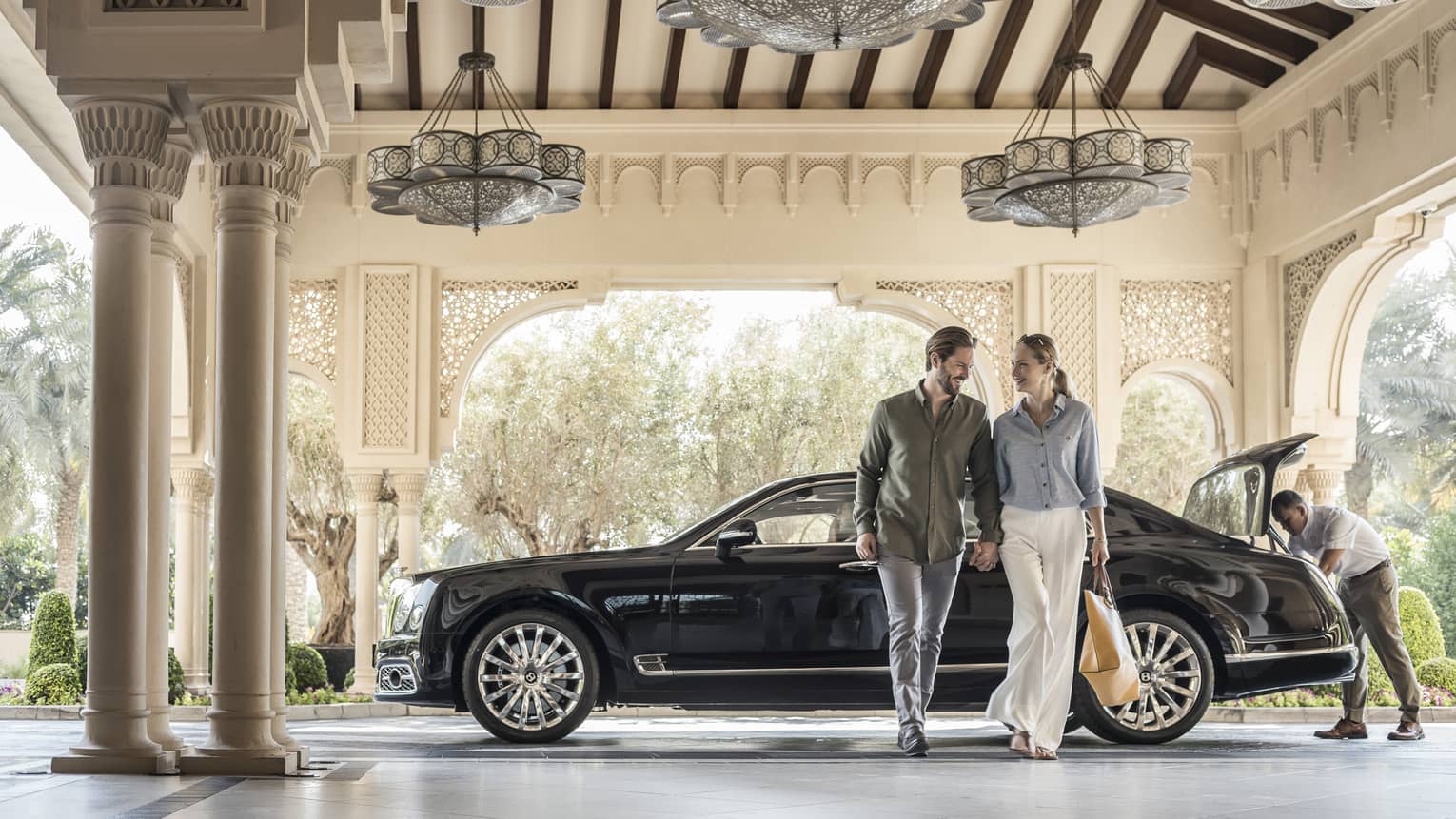 Couple holds hands, walks away from luxury car at entrance to Four Seasons Dubai at Jumeirah Beach