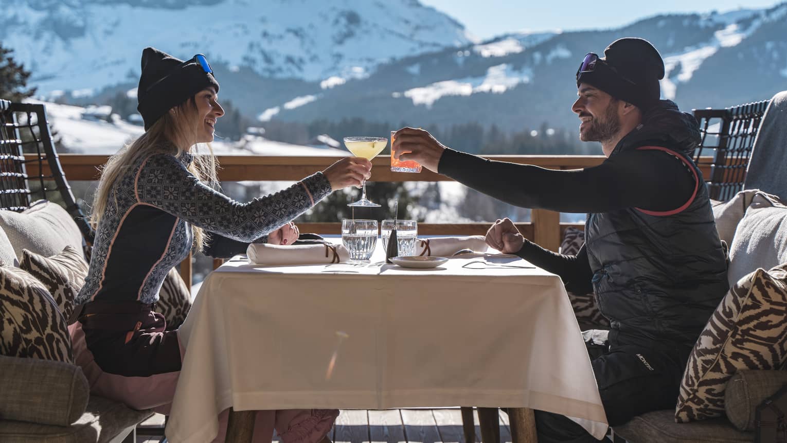Two people drinking on a patio outside with snowy mountains in the distance