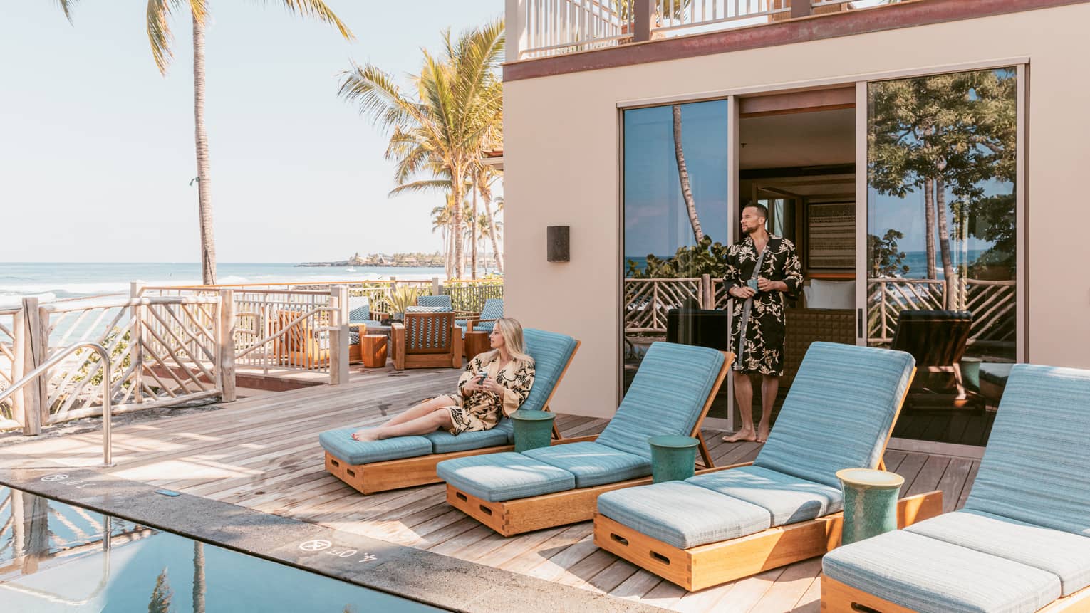Private pool terrace, woman sits on one of four sun loungers with turquoise cushions
