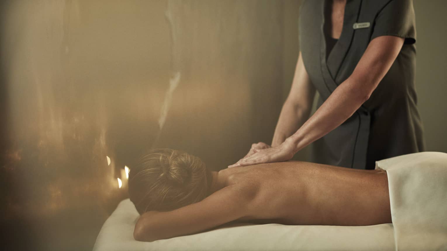 A woman laying on a massage bed being given a massage by a staff member.