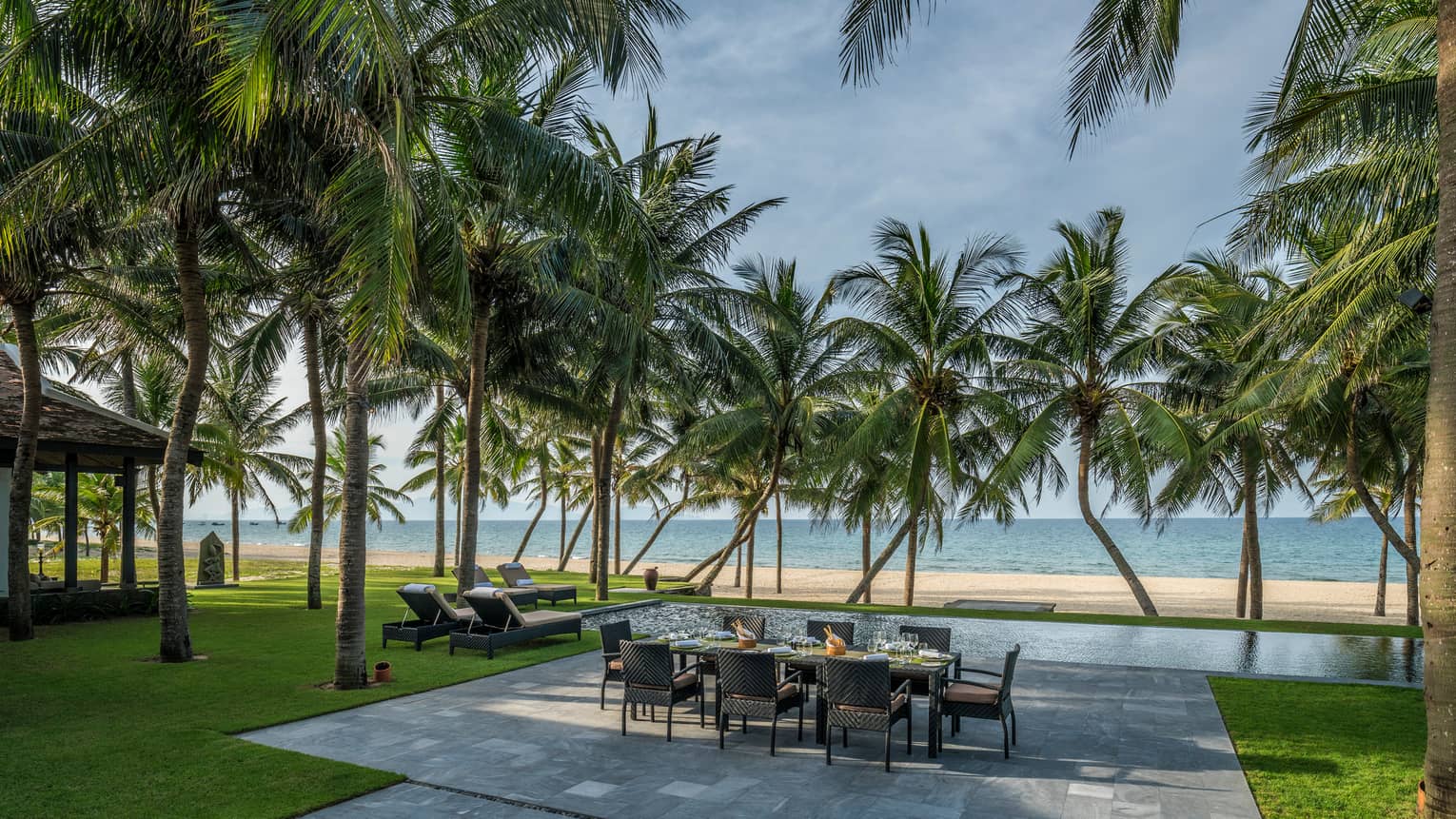 Beachfront Villa large stone patio with private dining table, lounge chairs under palms