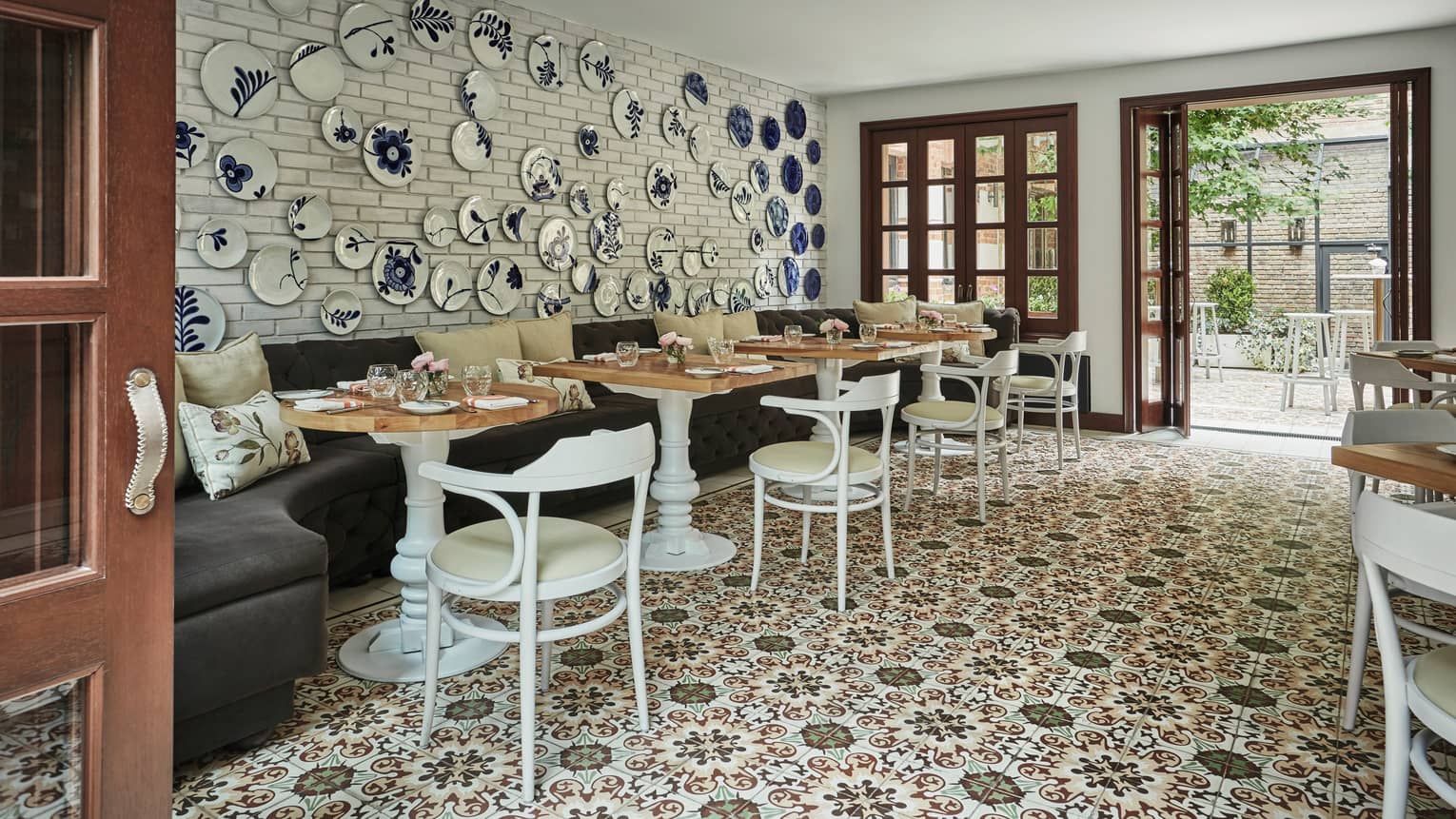 Blue-and-white decorative plates on wall over velvet banquette, cafe tables and chairs, tile floor