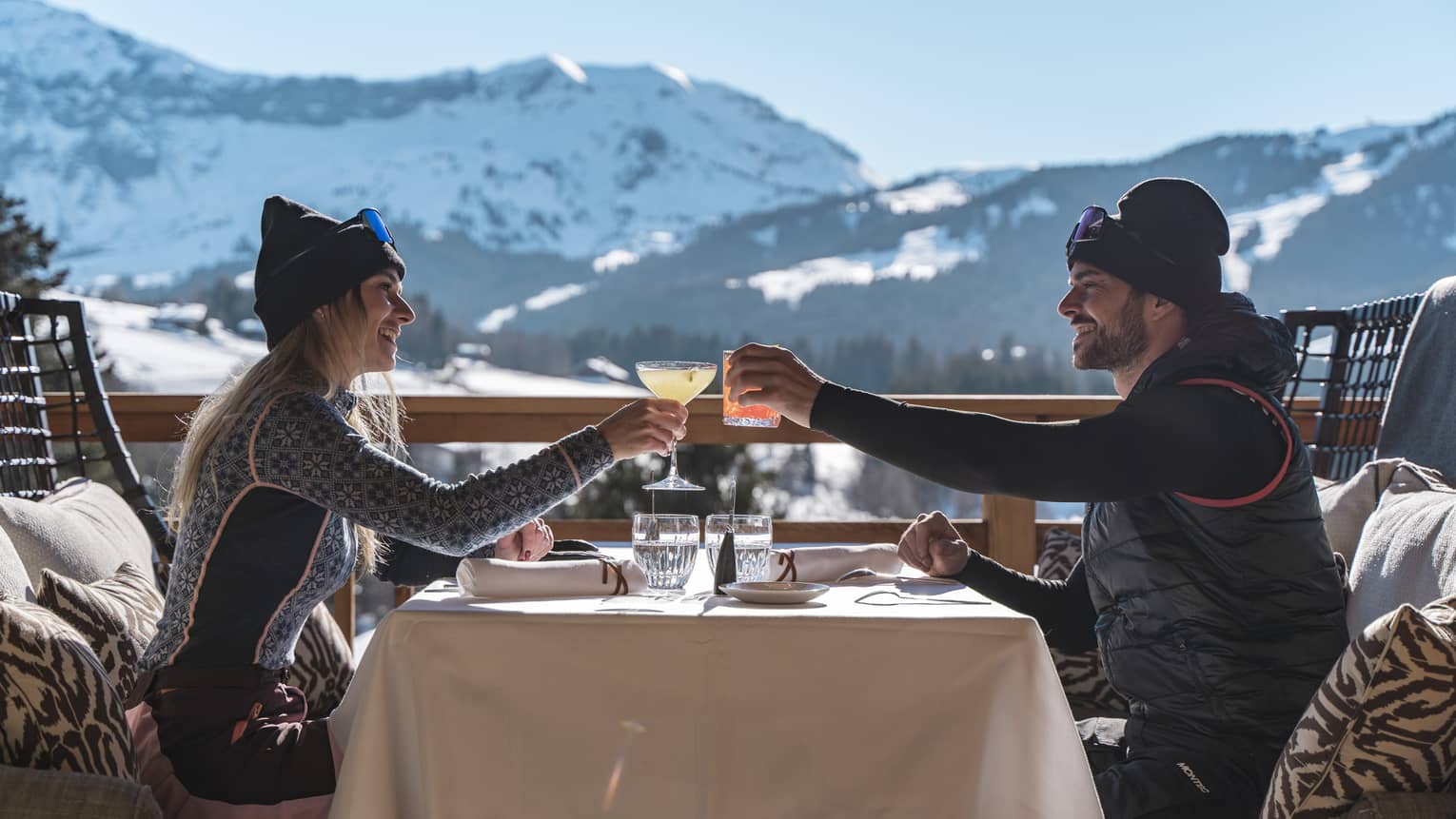 Two people drinking on a patio outside with snowy mountains in the distance