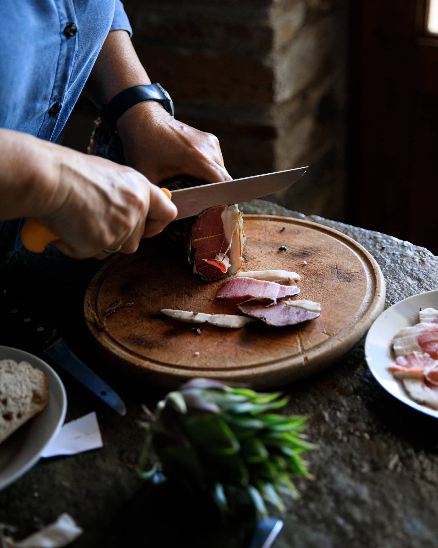 Person cutting Louza (Aegean prosciutto) on round cutting board