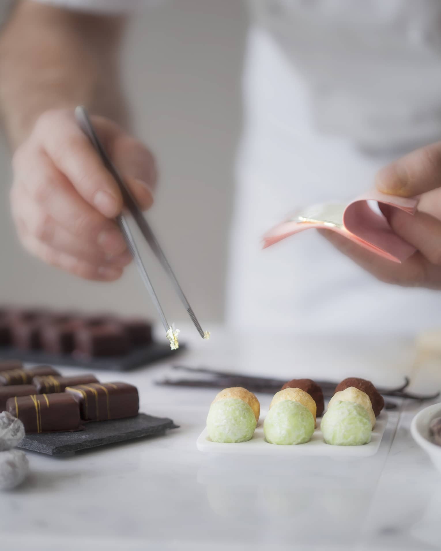 A close up of a male chef's hands using tongs to place various chocolates on parchment paper