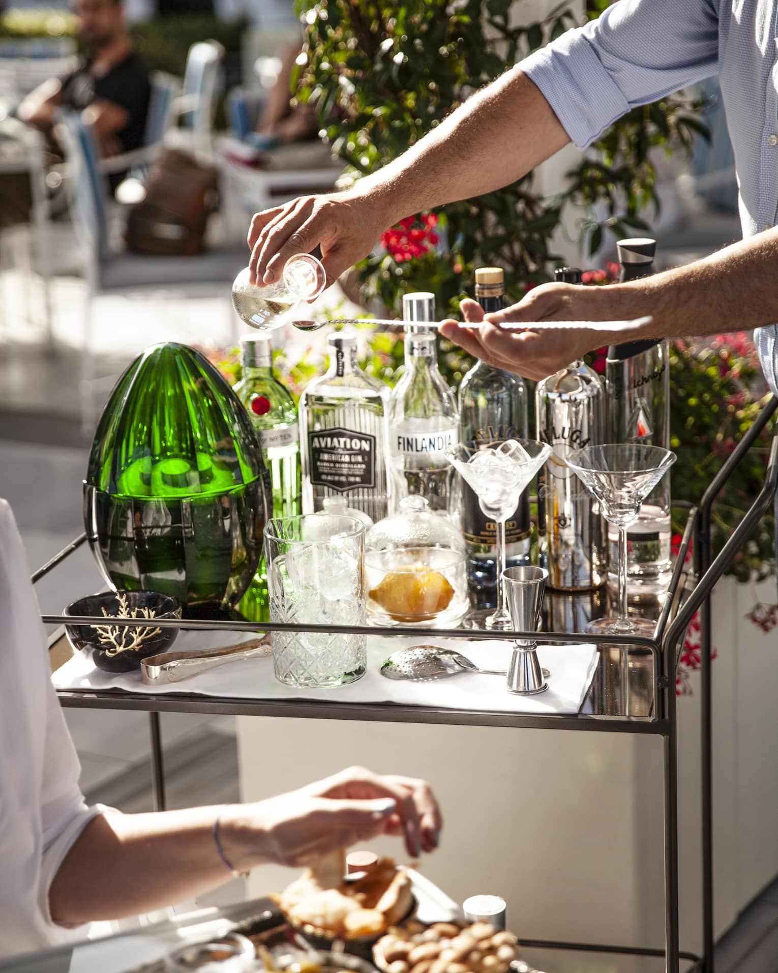Man pours a drink at outdoor cocktail service cart with various glass bottles