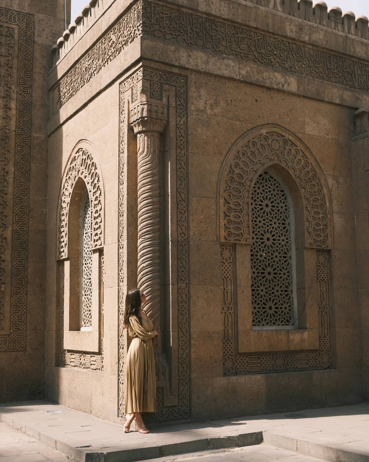 A guest looks up at an ornately carved building featuring a spiral column and arched windows with honeycomb latticework.