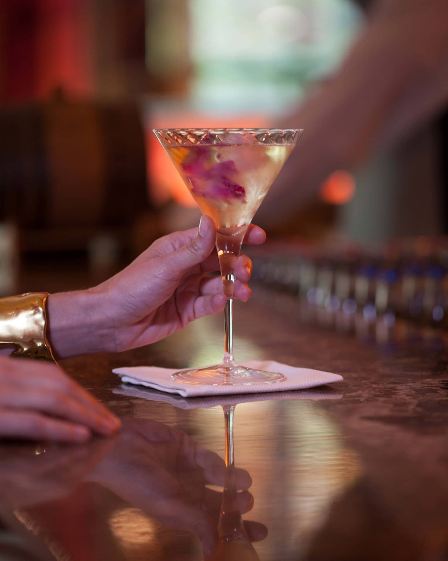 Close-up of hand of woman wearing gold cuff, holding martini glass on bar 