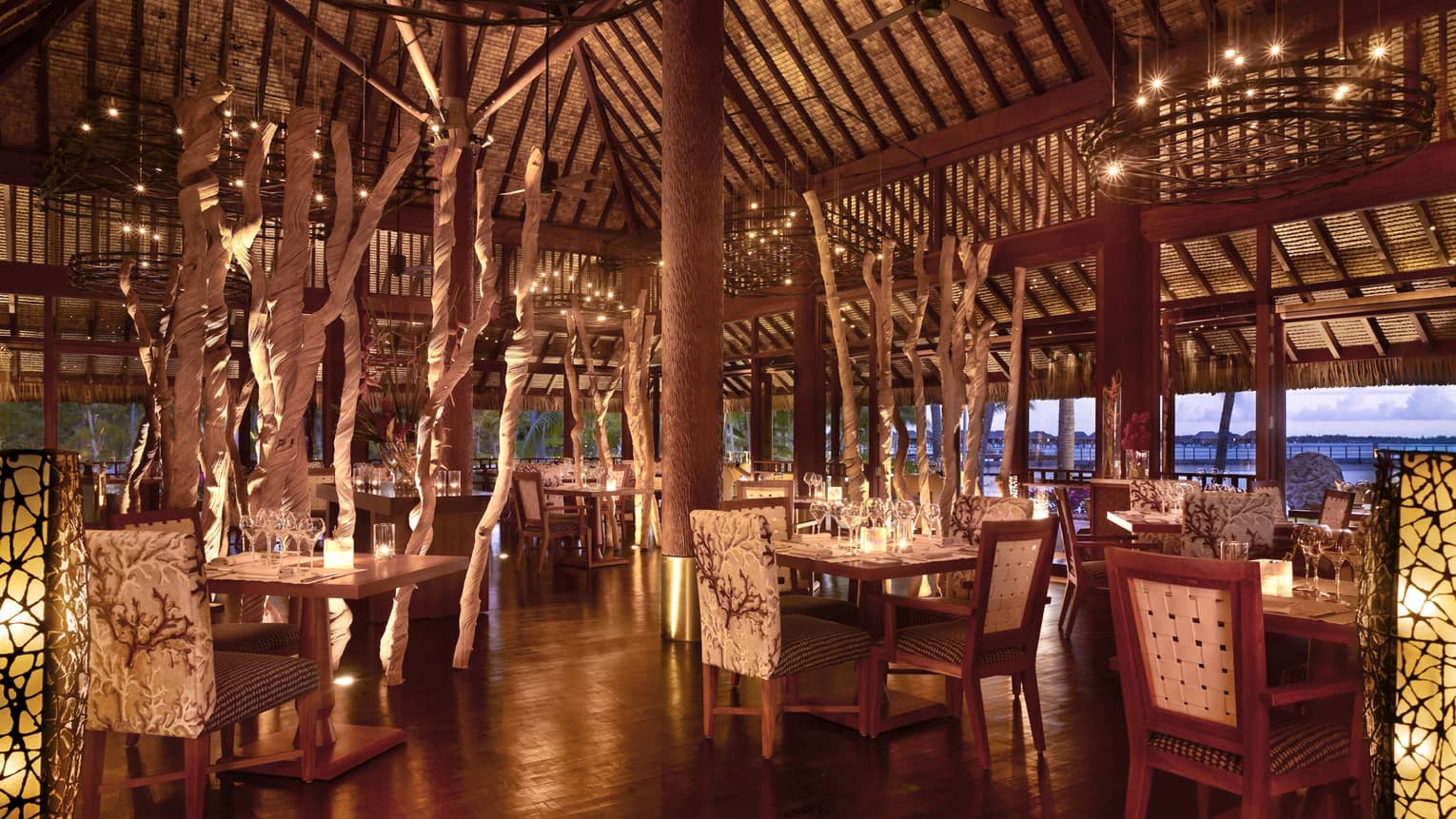 Elegant, candle-lit Arii Moana open-air dining room with plush chairs, decorative branches 