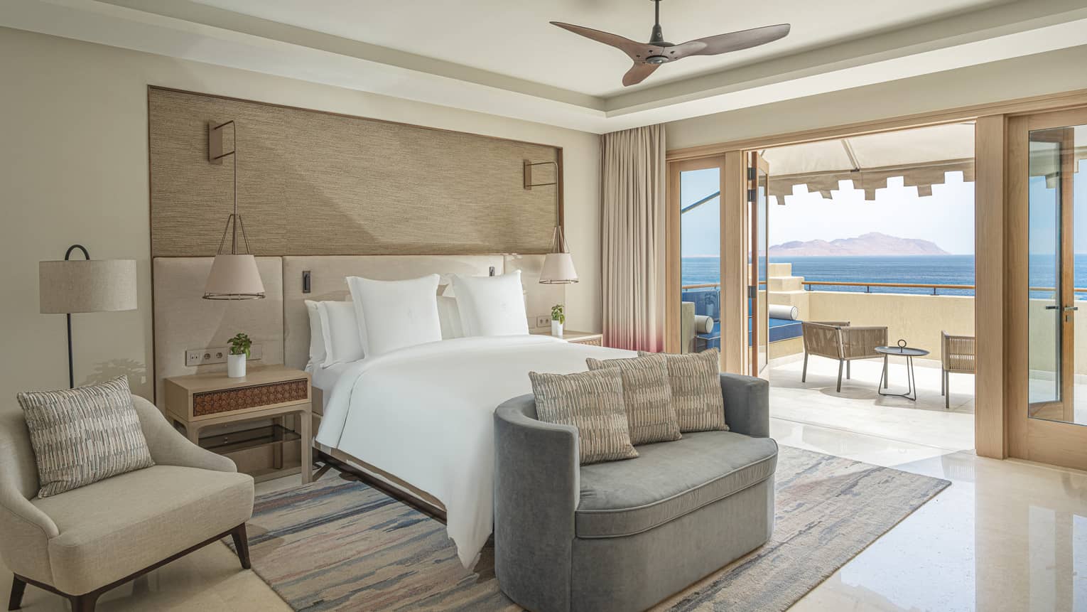 Four Seasons Suite bedroom with foot-of-the-bed chaise longue, arm chair, doorway to terrace with sea views