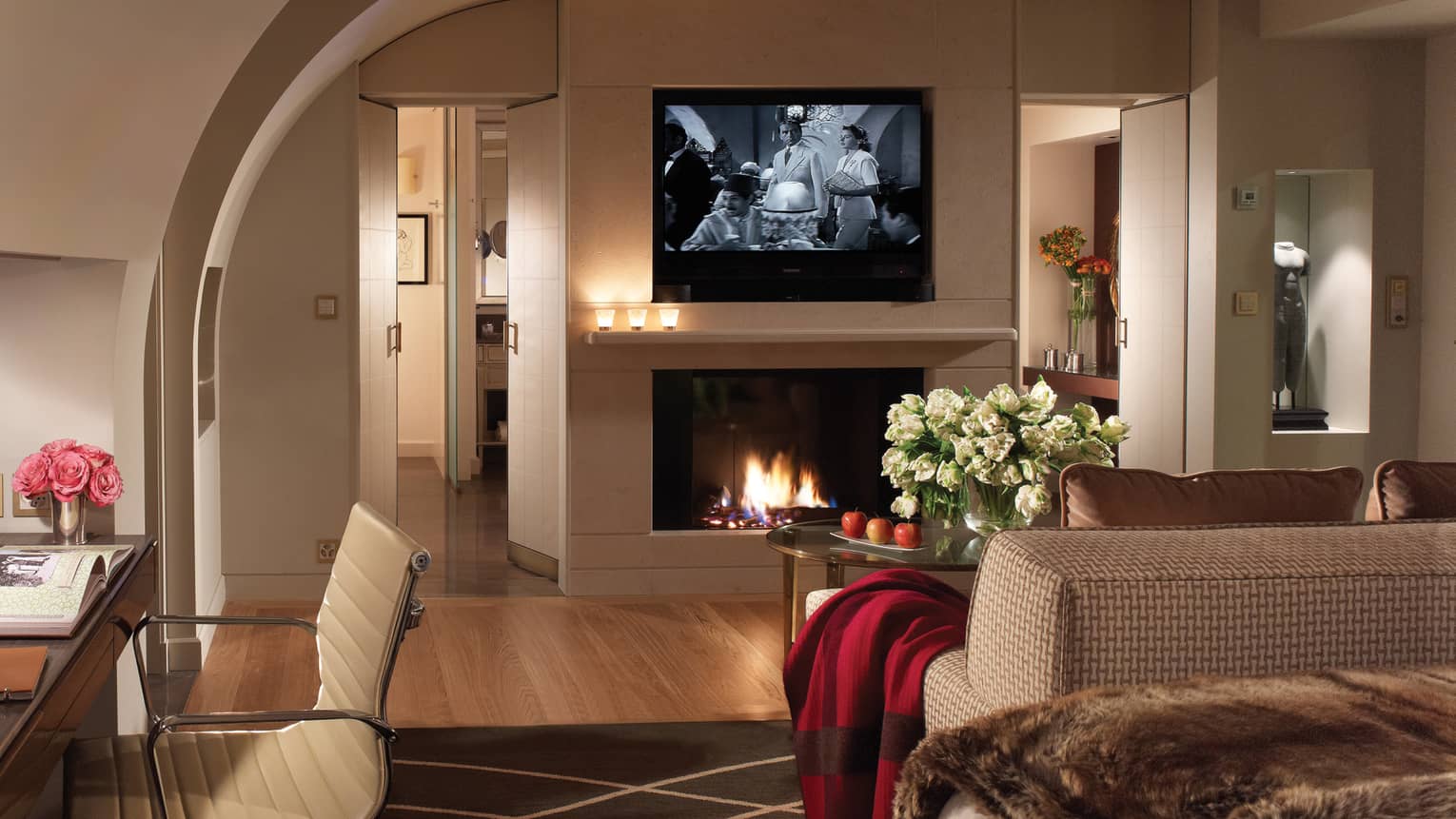 Flat-screen TV showing black-and-white-movie above glass fireplace, sofa with red blanket on arm