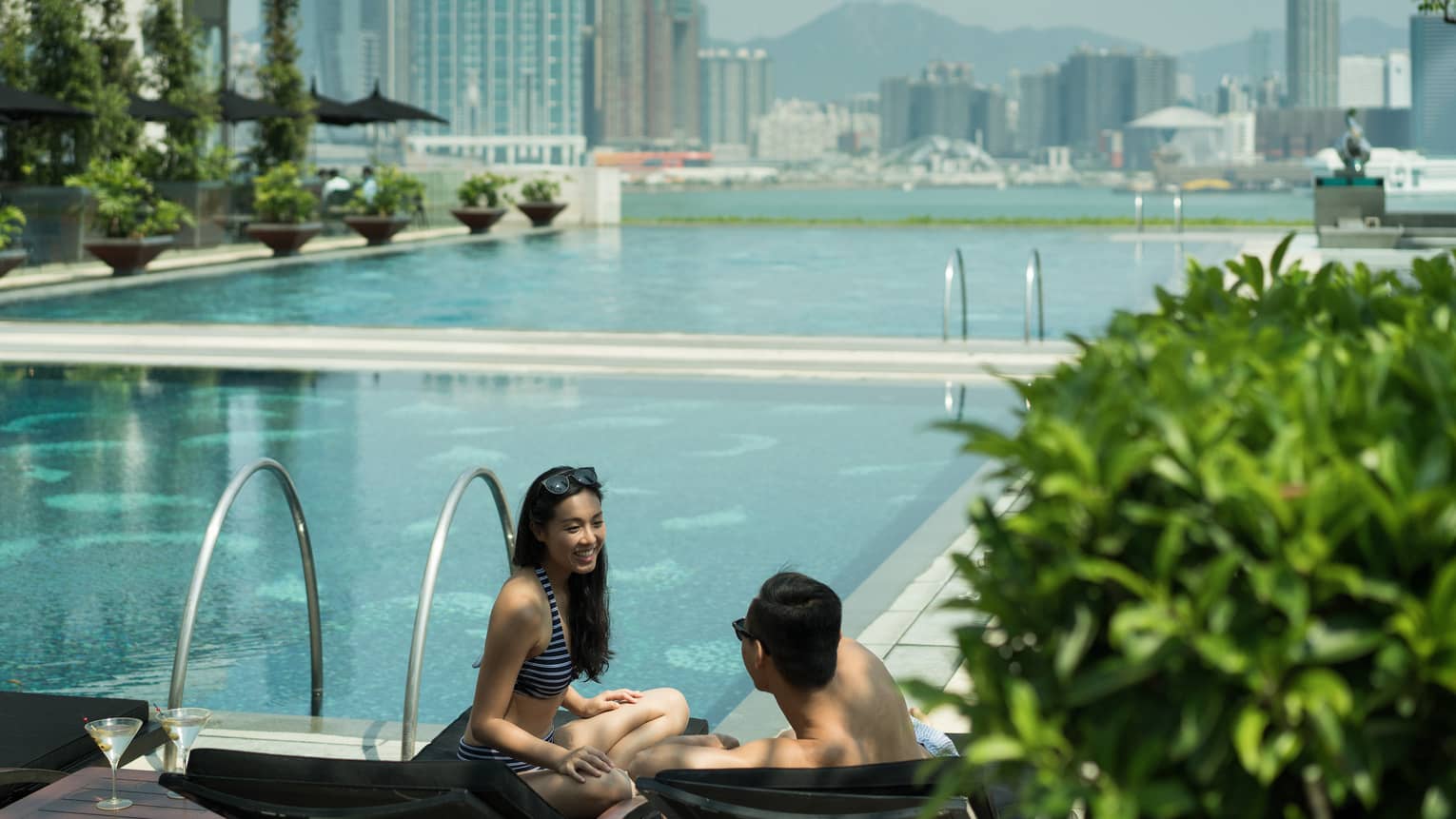 Couple wearing swimsuits on outdoor swimming pool deck, city skyline in background