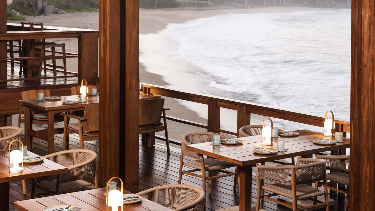 Wooden tables and chairs with small lanterns on restaurant terrace, next to the beach