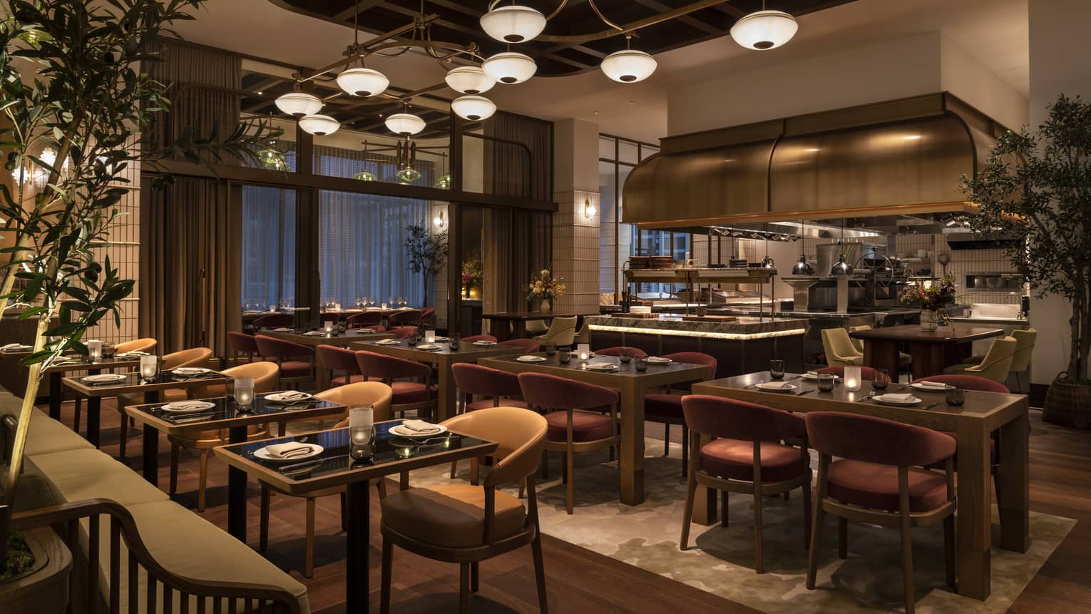 A dining outlet that is dimly lit with brown wooden chairs, tables and an open kitchen.