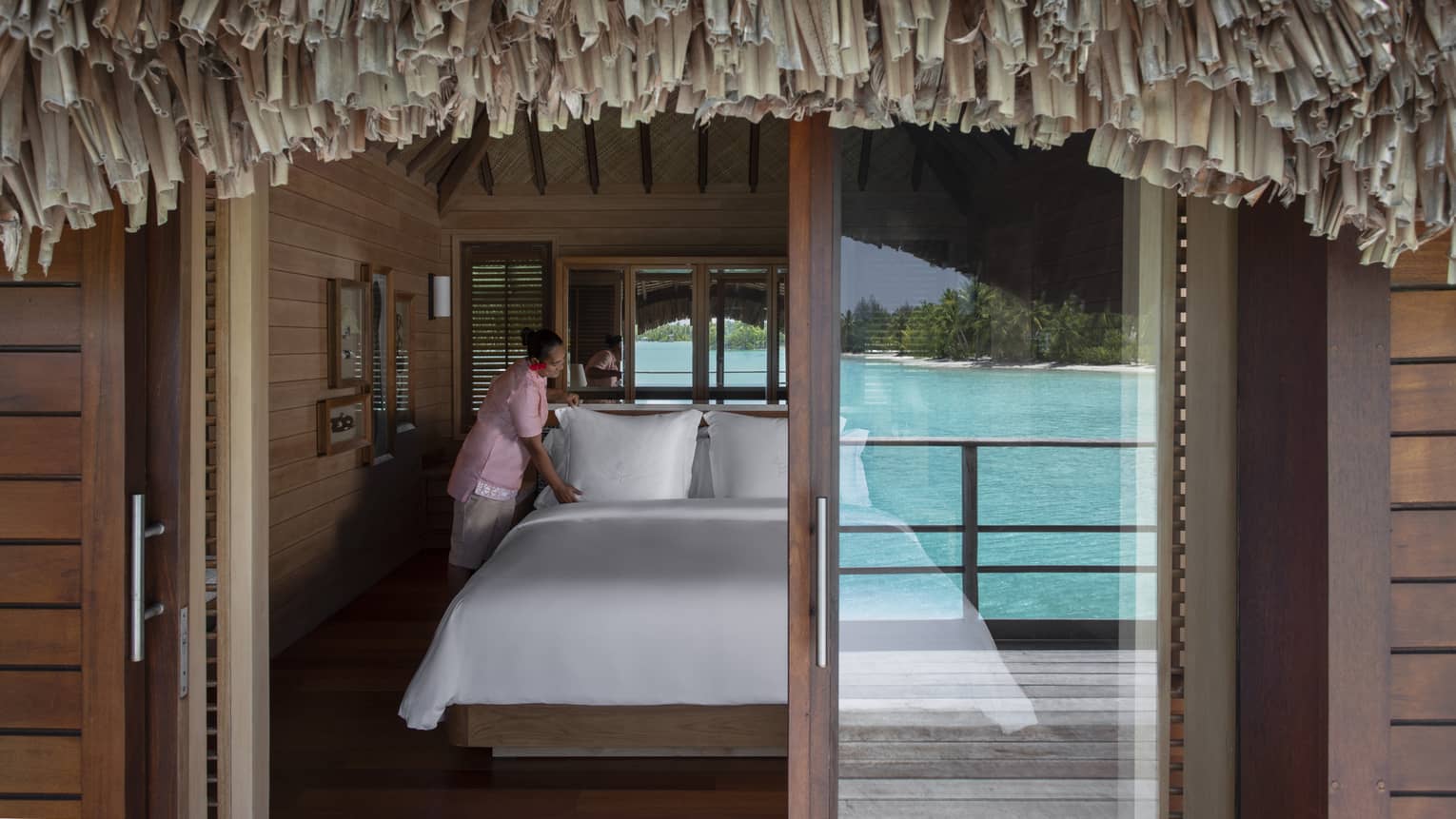 View through overwater bungalow sliding glass door to hotel bed 