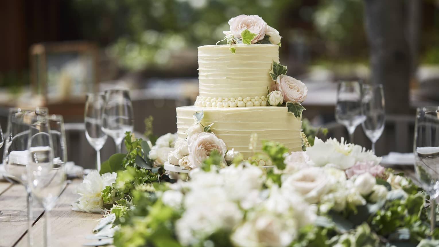 Two-tiered white wedding cake on banquet table with wine glasses, flowers