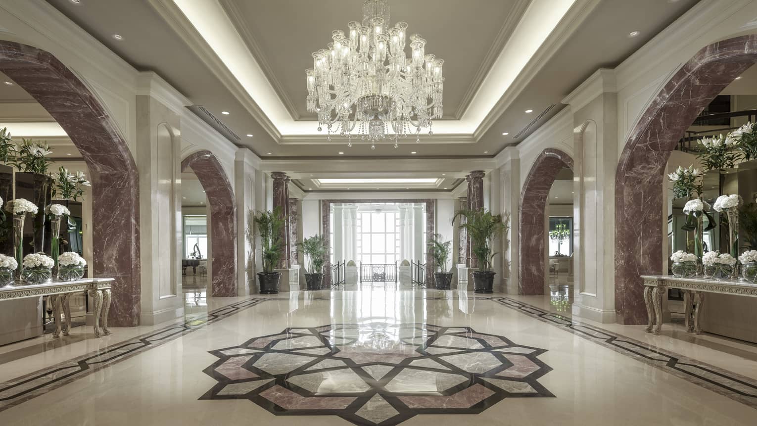 The marble lobby with a crystal chandelier above a mosaic.