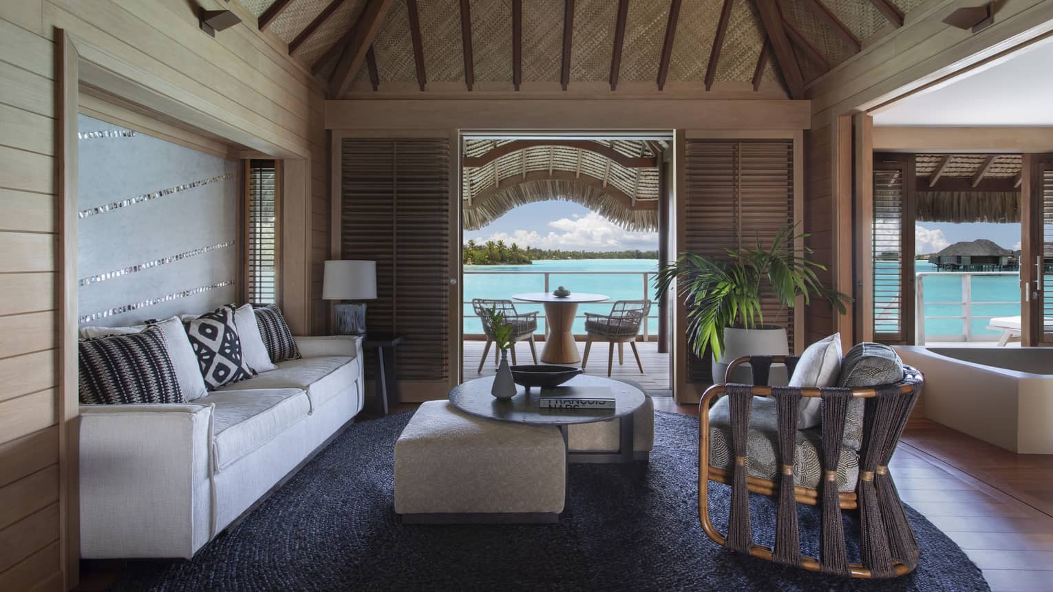 Living room with thatched roof, white sofa, arm chair, coffee table, view of turquoise lagoon