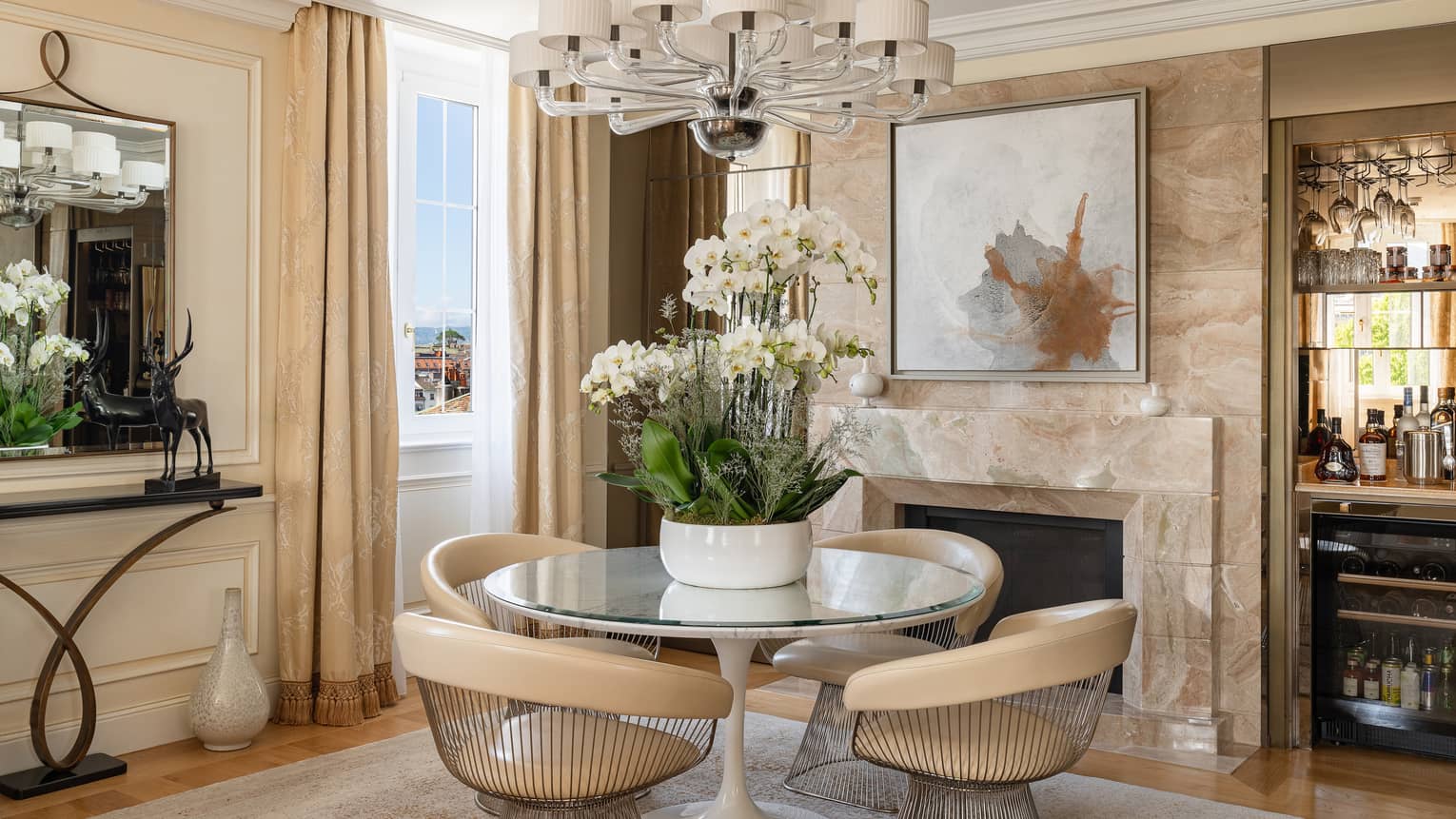 Elegant dining room with round table and four modern chairs, large floral arrangement, wet bar and fireplace, in the Presidential Suite at Four Seasons Hotel des Bergues, Geneva