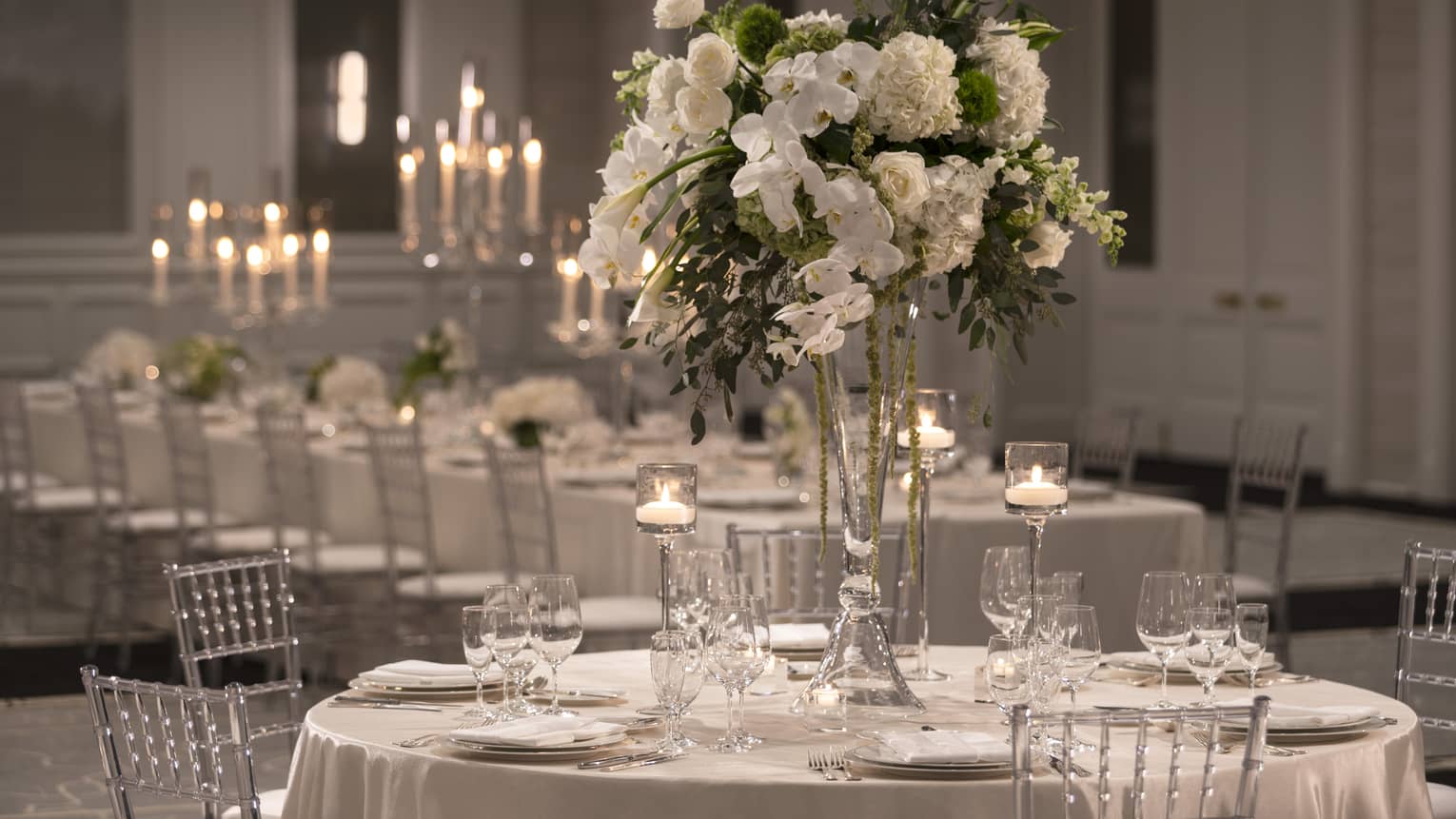 One formally set white rectangular table and candelabras, one round table and white floral centerpiece 
