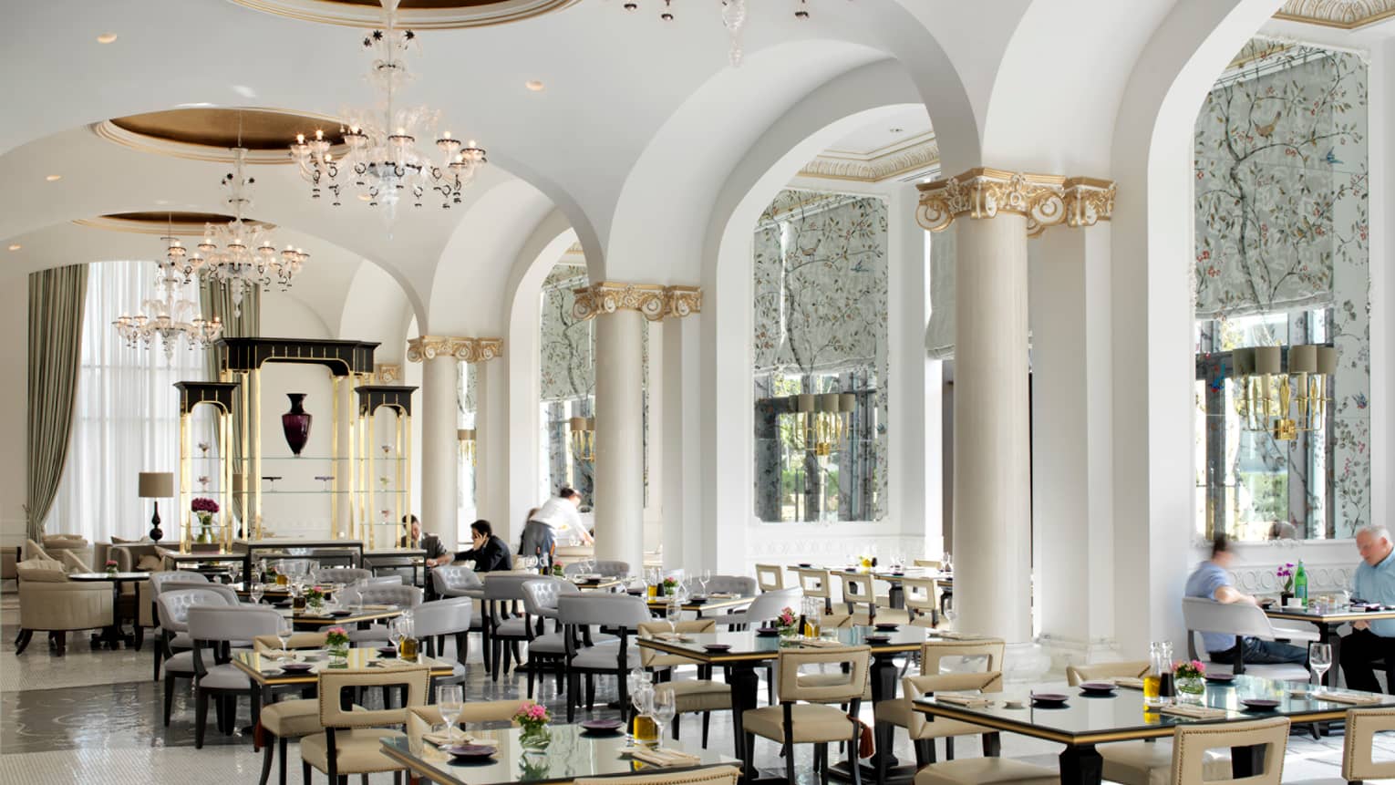 Bright Zafferano dining room with tall sweeping white ceiling, white pillars with decorative gold trim, tables and chairs below