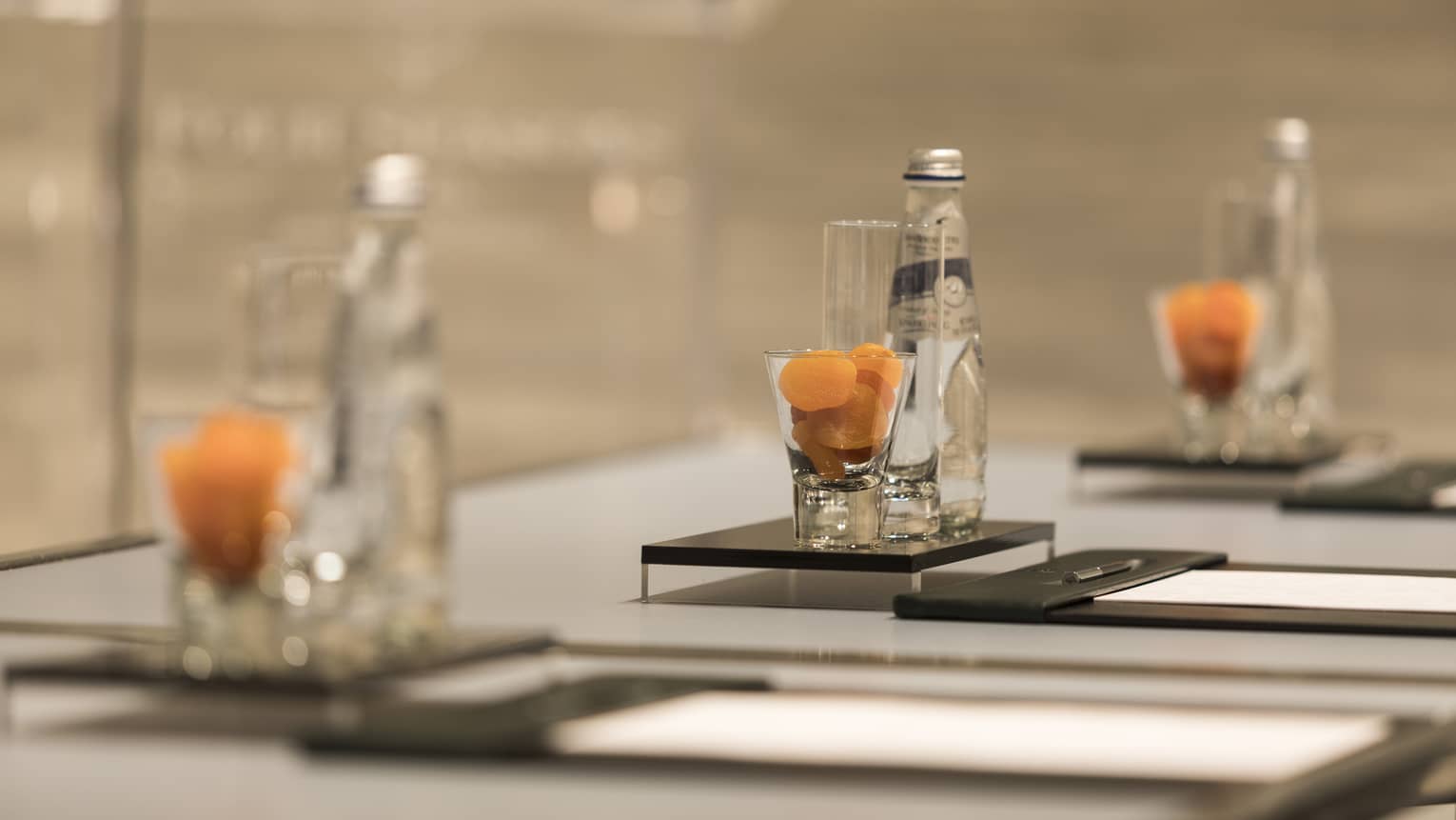 Close-up of meeting table place setting with agenda, dried apricots in glass, bottle of sparkling water