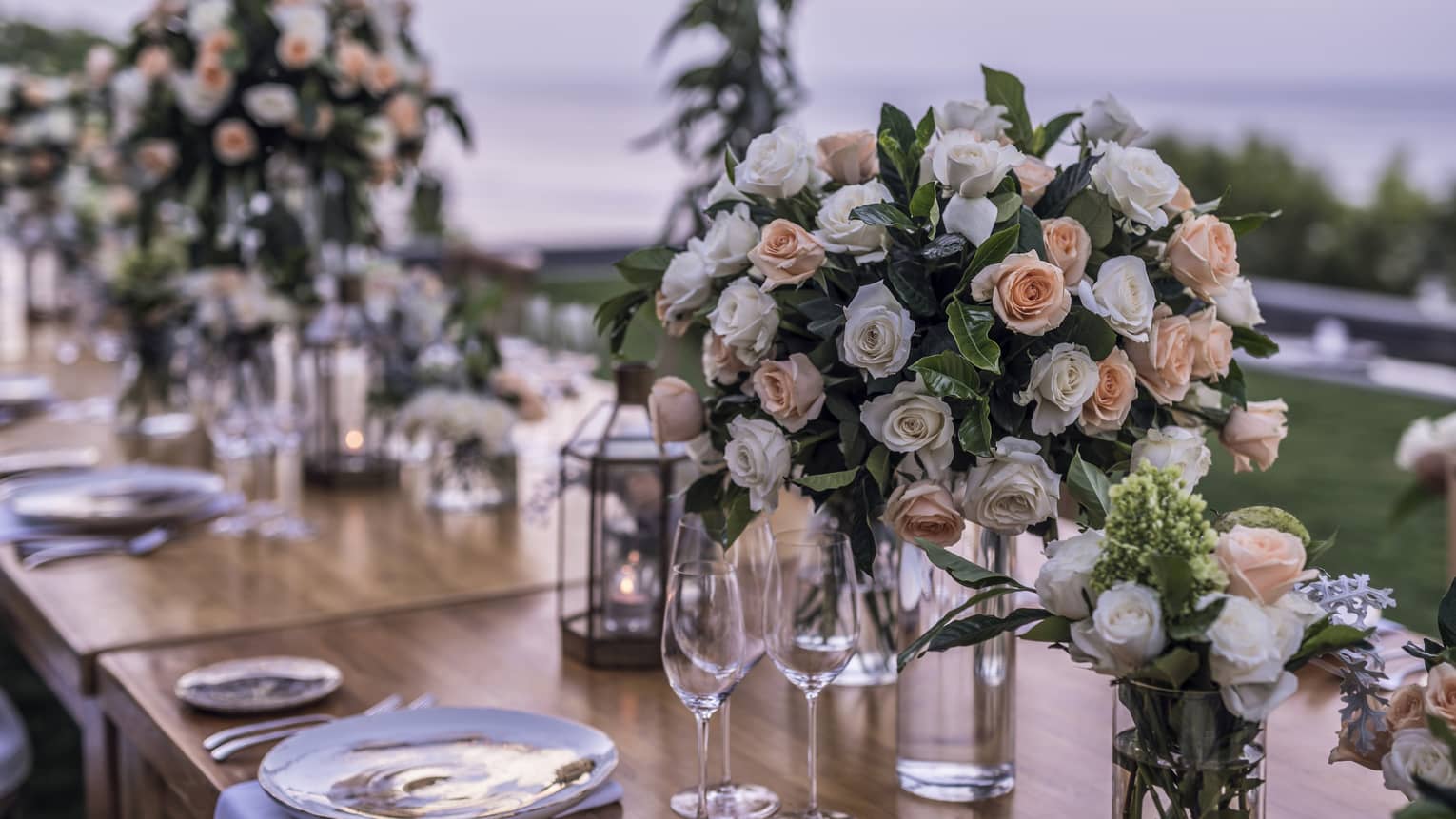 Pink and white roses in vases on long dining table at outdoor wedding reception