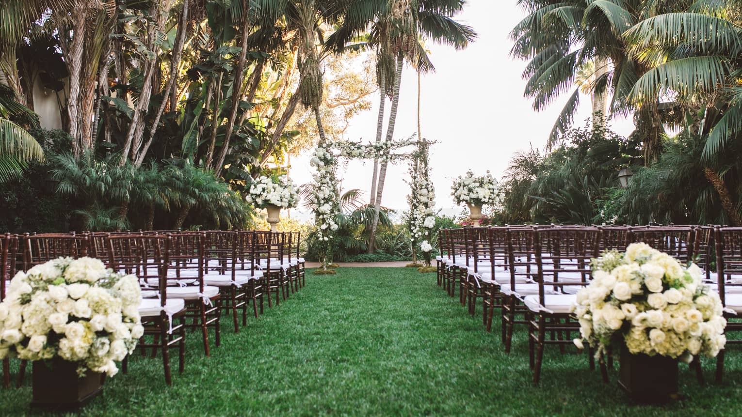Wedding on Mariposa garden lawn, white roses and rows of white chairs on sides of aisle to altar  